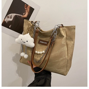 Detail of khaki canvas tote bag with leather strap, metal chain, and plush cloud charm