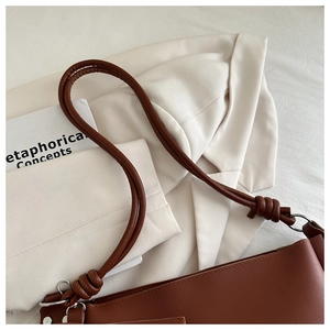 Detail of a brown leather shoulder bag featuring silver metal rings and knotted strap accents