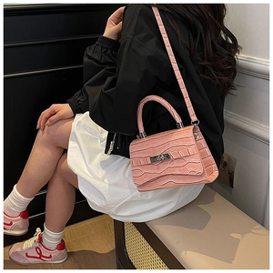 Pink crocodile-embossed shoulder bag with silver clasp and adjustable strap worn by model