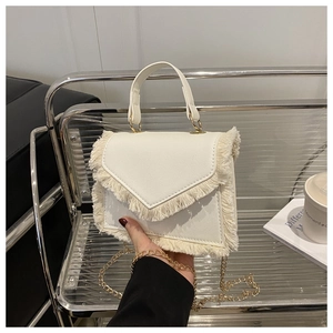 Close-up of white leather handbag featuring fringe trim and gold chain detail