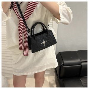 Detail of black woven texture handbag with silver star ornament worn by model