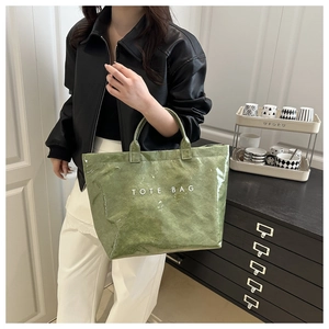 Close-up of green crinkled tote bag with TOTE BAG lettering held by a model