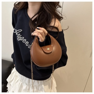 Detail of brown half-moon shoulder bag featuring gold chain strap and smooth leather texture