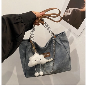 Detail of blue denim tote with leather straps, chain detail and plush cloud charm