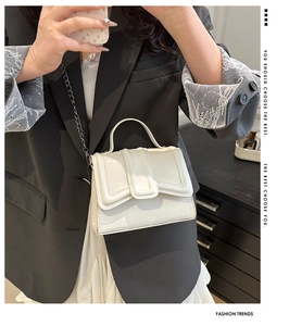 Detail of white crocodile embossed mini bag with chain strap on a black blazer
