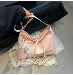 Close-up of pink leather tote bag featuring a white lace bow and pearl heart charm accessory