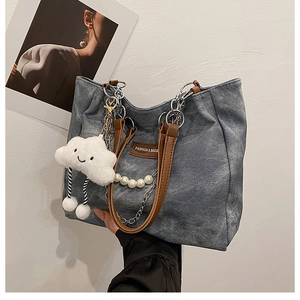 Detail of blue denim tote bag with brown leather tag, silver chain, and pearl strap