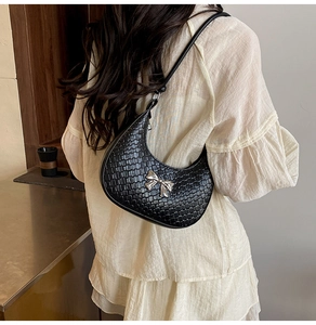 Detailed close-up of black woven crescent bag with silver metallic bow and leather strap