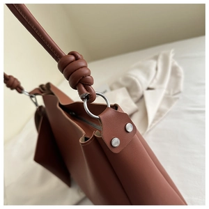 Detail of woven knot handle and silver rivets on a caramel brown bucket bag