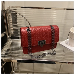 Detail of red chain bag showing woven texture, silver metal lock, and rectangular shape