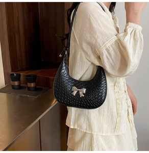 Close-up of black hobo bag with woven texture and a silver metal bow accent