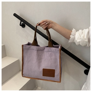 Close-up of purple corduroy tote bag showing striped texture and brown handle detail