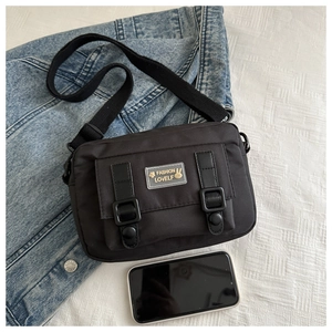 Macro shot of black nylon crossbody bag with flap and decorative buckles on denim surface