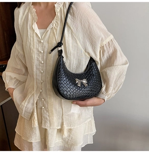 Close-up of black crescent shoulder bag featuring silver bow detail and textured finish