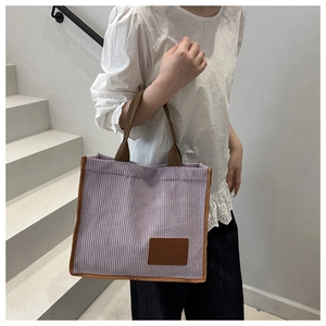 Detail of light purple corduroy bucket bag with contrast brown handle and fashion label