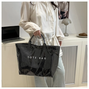 Detail of a black glossy tote bag with white text held by a model in a cozy interior