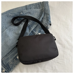 Close-up of black nylon crossbody bag with adjustable strap on denim jacket backdrop