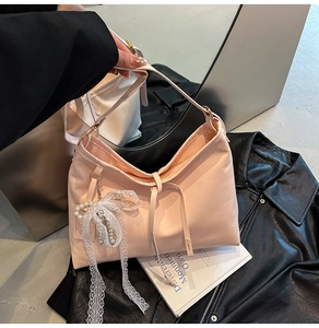 Detail of pink faux leather tote bag with lace bow and pearl pendant on black leather