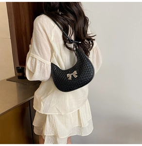 Detail of black woven crescent bag with silver bow ornament worn with white dress
