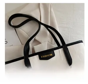 Close-up of a white tote bag featuring black leather handles and gold Fashion lettering