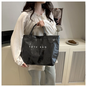 Detail of a large black patent leather tote bag with bold TOTE BAG print for daily commute
