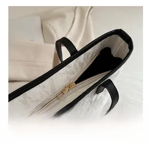 Detail view of smooth metal zipper and black leather handles on white textured tote bag