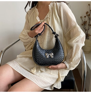 Detail of black woven crescent bag with silver metal bow and knotted shoulder strap
