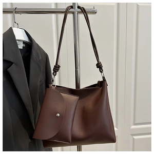 Detail of dark brown tote bag with small pouch and knotted strap on wooden door