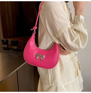 Detail of pink croc-embossed crescent bag with silver bow buckle on model