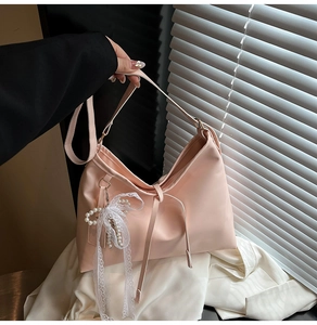 Detail of pink satin hobo bag featuring lace bow and pearl bead pendant accessories