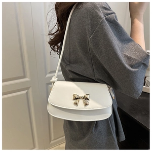 Detail of white leather shoulder bag featuring a decorative gold bow clasp and sleek strap