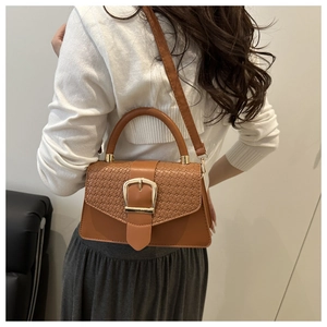 Detail of woven texture flap and golden buckle on a brown leather crossbody bag