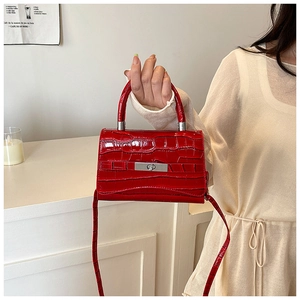 Close-up of bright red crocodile textured handbag with silver twist lock on top handle
