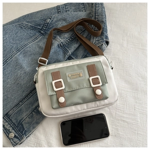 Detail of sage green canvas crossbody bag featuring phone size reference and buckle pockets