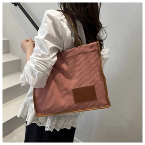 Detail of pink corduroy tote bag with leather logo patch and brown fabric shoulder strap