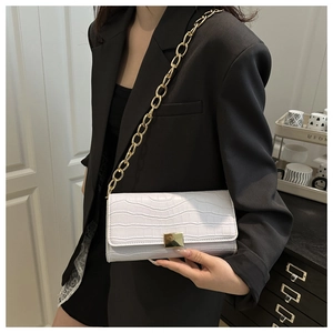 Détail du sac à bandoulière blanc à motif crocodile avec chaîne dorée sur blazer noir