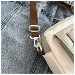 Detail of adjustable shoulder strap and plastic buckle on cream nylon crossbody bag