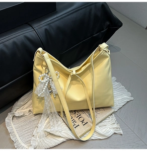 Detail of pale yellow leather tote bag featuring a pearl and lace bow pendant accessory
