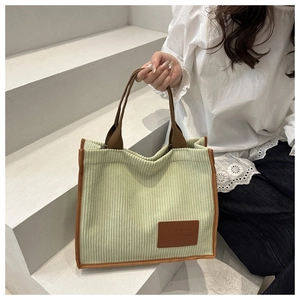 Detailed texture of green corduroy tote bag with brown straps and leather logo tag