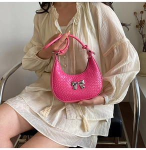Detail of pink woven half-moon handbag with silver metal bow and knotted handle detail