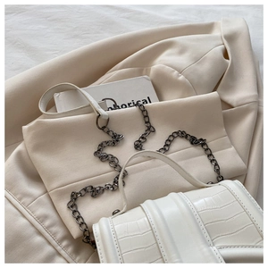 Détail du sac à main blanc à motif crocodile avec chaîne argentée sur un blazer blanc