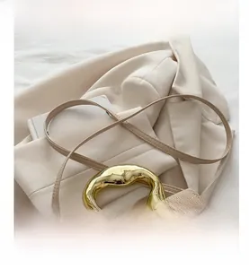 Detail of beige woven handbag featuring a unique gold metal handle and slim leather strap