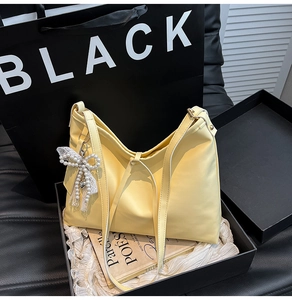 Close-up of yellow leather Hobo bag with pearl bow pendant inside a black gift box