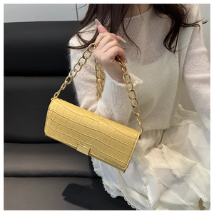 Détail du sac baguette jaune à motif crocodile avec chaîne dorée portée par un mannequin