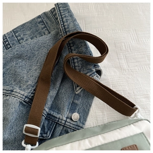 Detail of the green nylon crossbody bag showing the fabric texture and brown shoulder strap