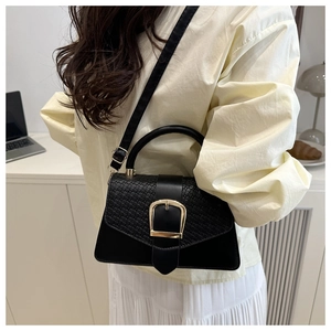 Detail of black crossbody bag featuring crocodile texture flap and gold metal buckle