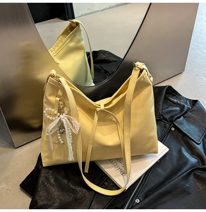 Detail of light yellow PU leather tote bag with elegant pearl lace bow charm on dark leather