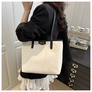 Close-up of white pleated tote bag with black straps and fashion label on a shoulder