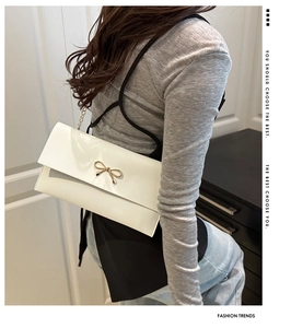 Detail of white leather envelope bag featuring a gold bow buckle and elegant metal chain