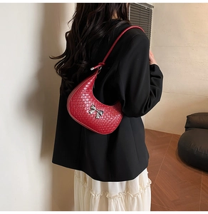 Detail of red woven crescent shoulder bag with silver bow on model in chic outfit